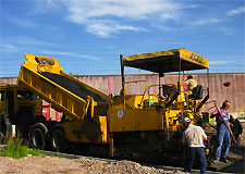 mehrere Arbeiter bei gelbem LKW der Teer abkippt zur Verarbeitung von Asphaltbelag